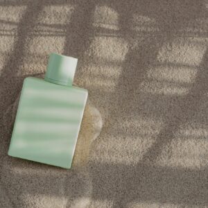 A sleek perfume bottle placed on sand with dramatic sunlight and shadow patterns, perfect for stylish product presentations.